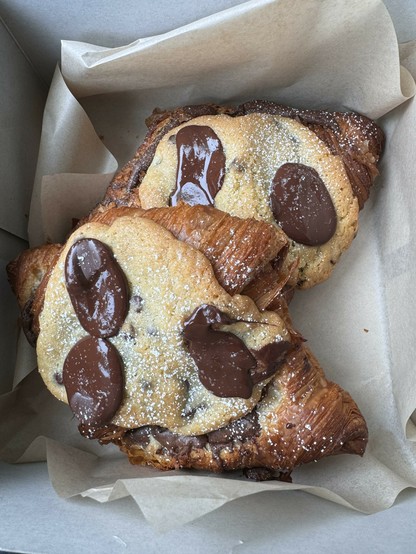 A pair of fresh, flaky butter croissants topped and filled with a combination of melty chocolate chip cookie dough and brownie batter