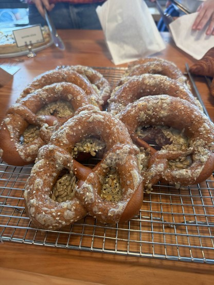 A couple rows of freshly baked pretzels covered in melted cheese and seeds, resting on a wire cooling rack